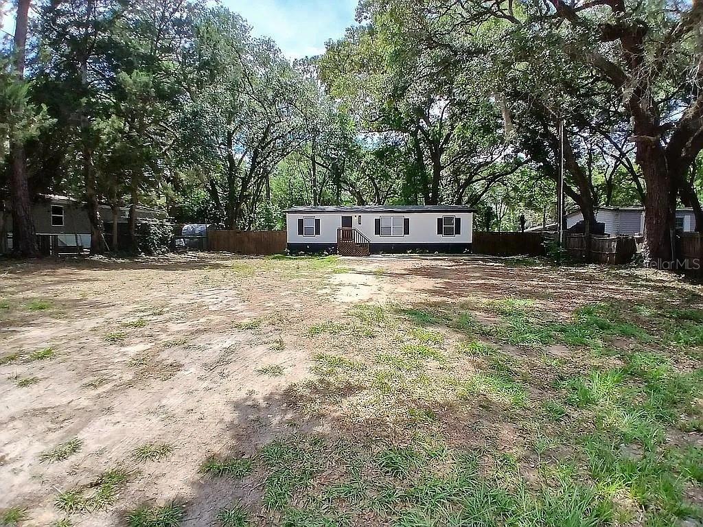 A single-story manufactured home sits on a large, mostly dirt lot surrounded by mature trees — 6626 NW 60 CT #9, OCALA, FL