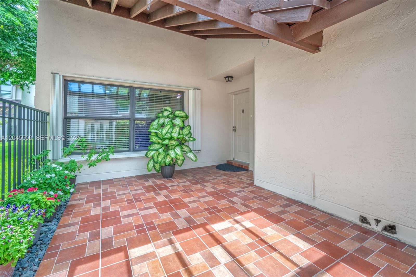 A covered patio features terracotta tile flooring, a large window, and a white entry door — 10060 SW 137th Ct, Miami FL 33186, MIAMI, FL