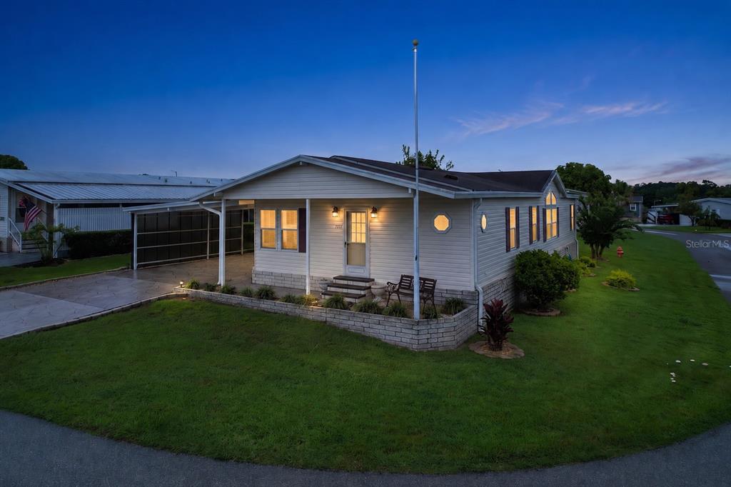 An exterior view of a single-story manufactured home with a carport and brick planter box — 1777 QUAIL HILL DRIVE, LAKELAND, FL