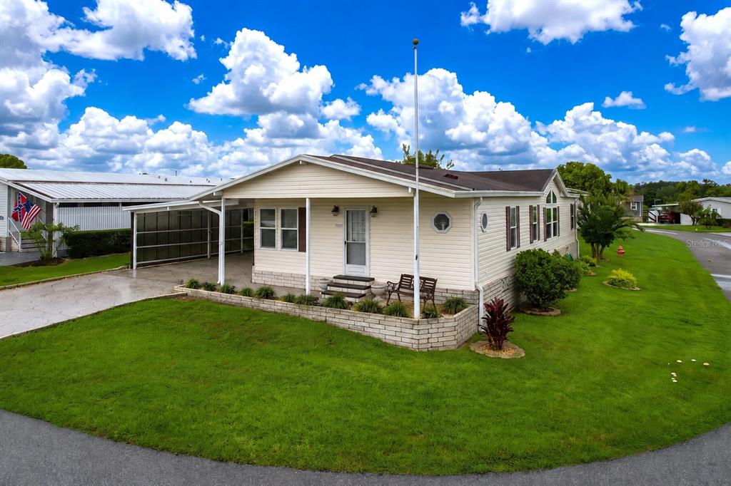 A single-story manufactured home with light siding, a carport, and a brick-bordered front garden — 1777 QUAIL HILL DRIVE, LAKELAND, FL