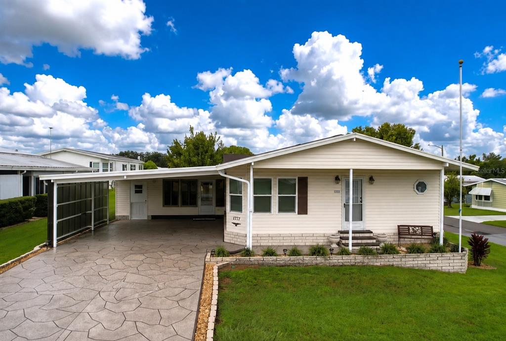 A single-story house with light siding, a covered carport, and a patterned concrete driveway — 1777 QUAIL HILL DRIVE, LAKELAND, FL