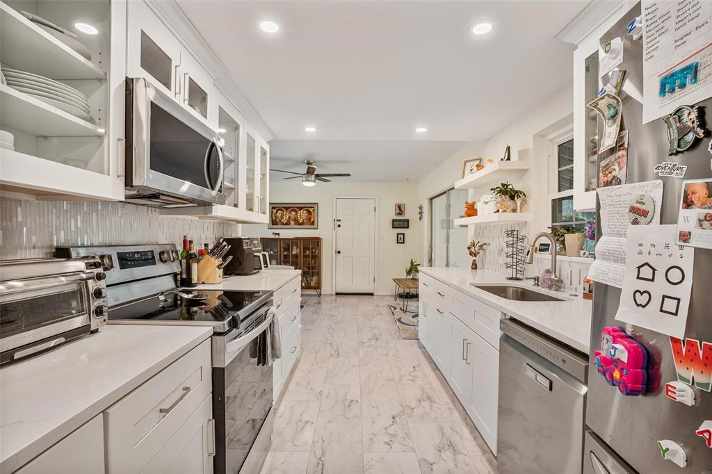 A galley kitchen features white cabinets, stainless steel appliances, and marble-look tile flooring — 2464 LYDIA WAY, NEW SMYRNA BEACH, FL