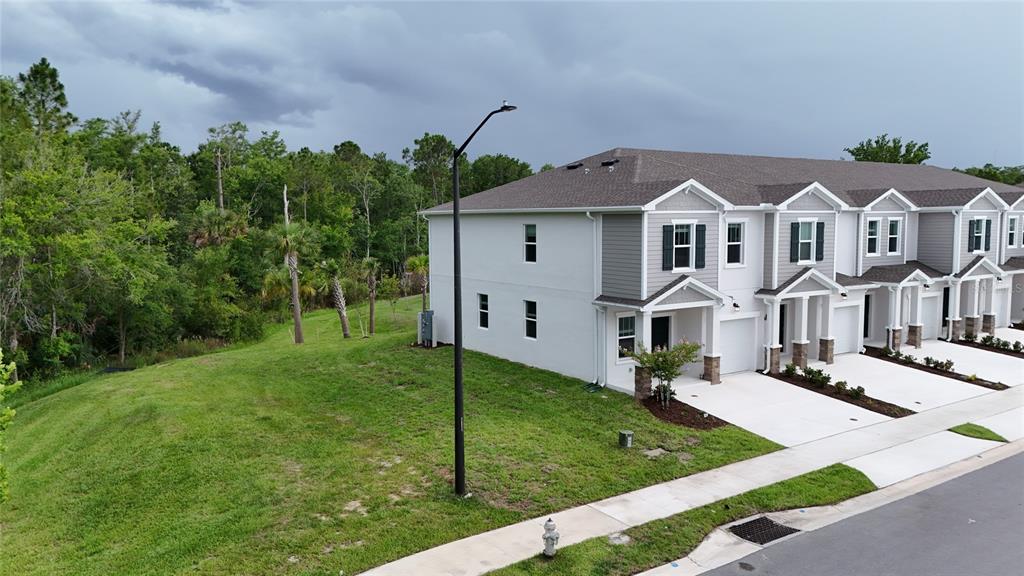 An aerial view of a multi-unit townhouse exterior with a grassy side yard and woods — 3091 CHROMATIC STREET, KISSIMMEE, FL