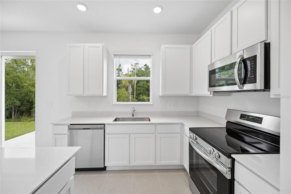 A modern kitchen features white cabinets, stainless steel appliances, quartz countertops, and a backyard view — 3091 CHROMATIC STREET, KISSIMMEE, FL