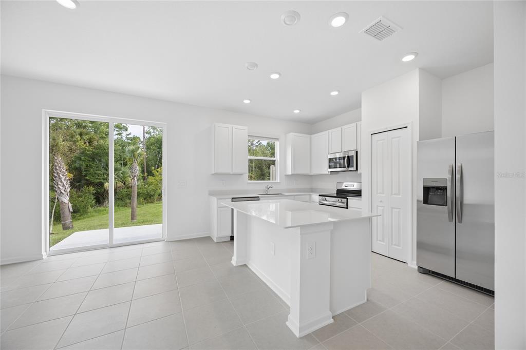 A modern kitchen features white cabinetry, a central island, stainless steel appliances, and sliding doors — 3091 CHROMATIC STREET, KISSIMMEE, FL