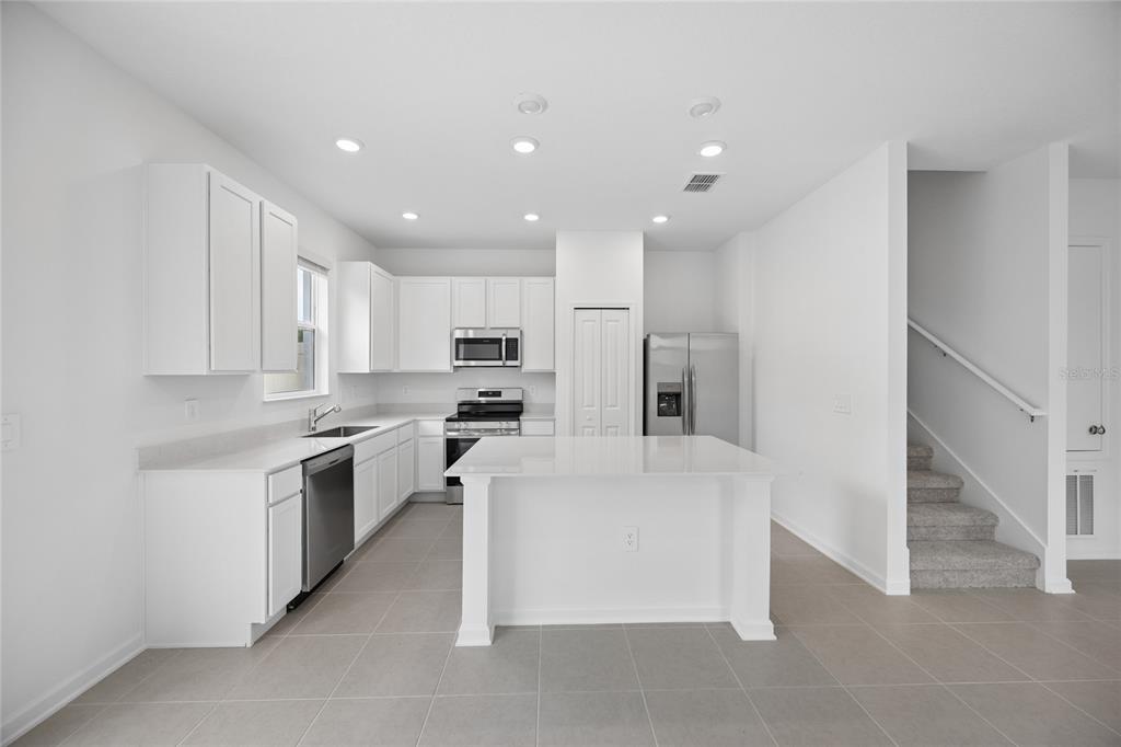 A modern kitchen features white cabinets, stainless steel appliances, a center island, and tile flooring — 3091 CHROMATIC STREET, KISSIMMEE, FL