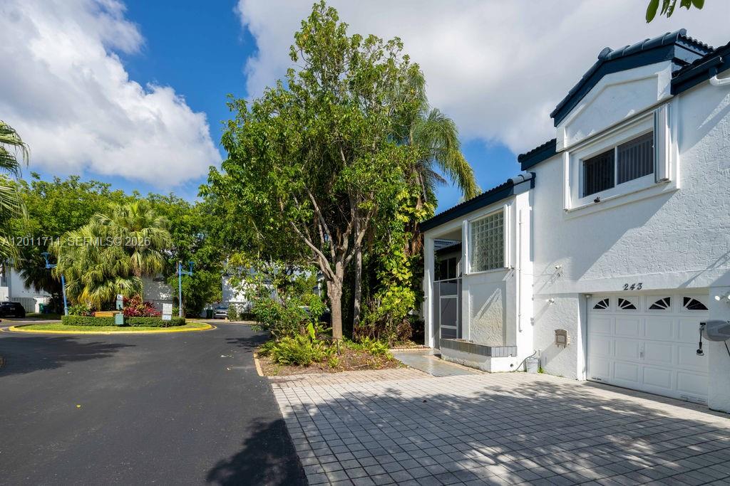 A white two-story townhouse with a garage and a paved driveway sits beside a tree — 243 NE 212th Ter, Miami FL 33179, MIAMI, FL