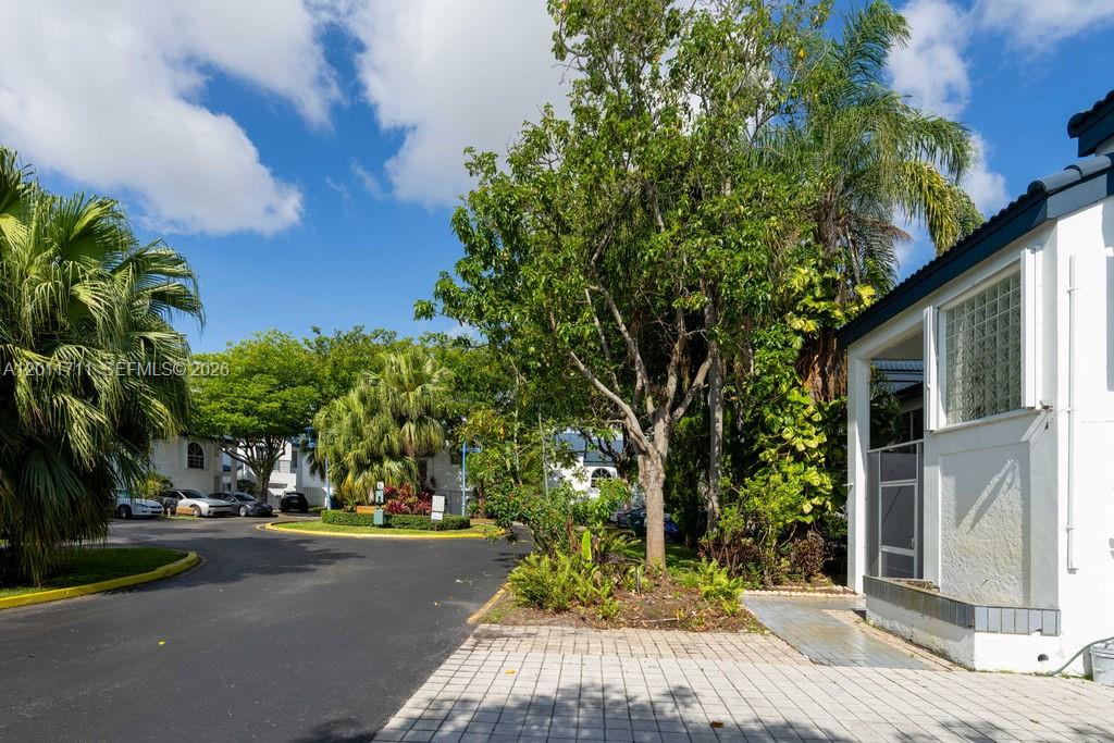 A paved driveway leads to a white building surrounded by lush trees and palm plants — 243 NE 212th Ter, Miami FL 33179, MIAMI, FL