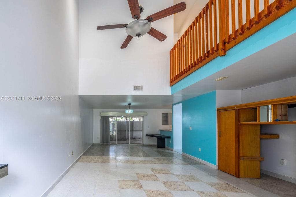A living room with a high ceiling, a wooden loft railing, and tiled flooring — 243 NE 212th Ter, Miami FL 33179, MIAMI, FL