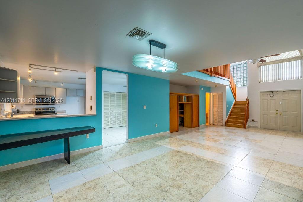 A bright living area features teal walls, tiled floors, a wooden staircase, and kitchen access — 243 NE 212th Ter, Miami FL 33179, MIAMI, FL