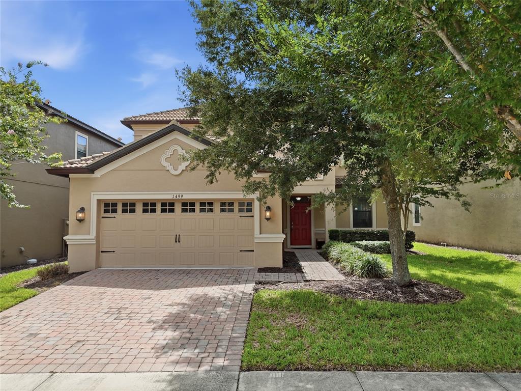 A two-story tan stucco house features a brick paver driveway and a red front door — 1499 ROLLING FAIRWAY DRIVE, DAVENPORT, FL