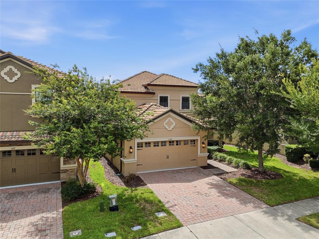 An exterior view of a two-story tan stucco house with a tiled roof and driveway — 1499 ROLLING FAIRWAY DRIVE, DAVENPORT, FL