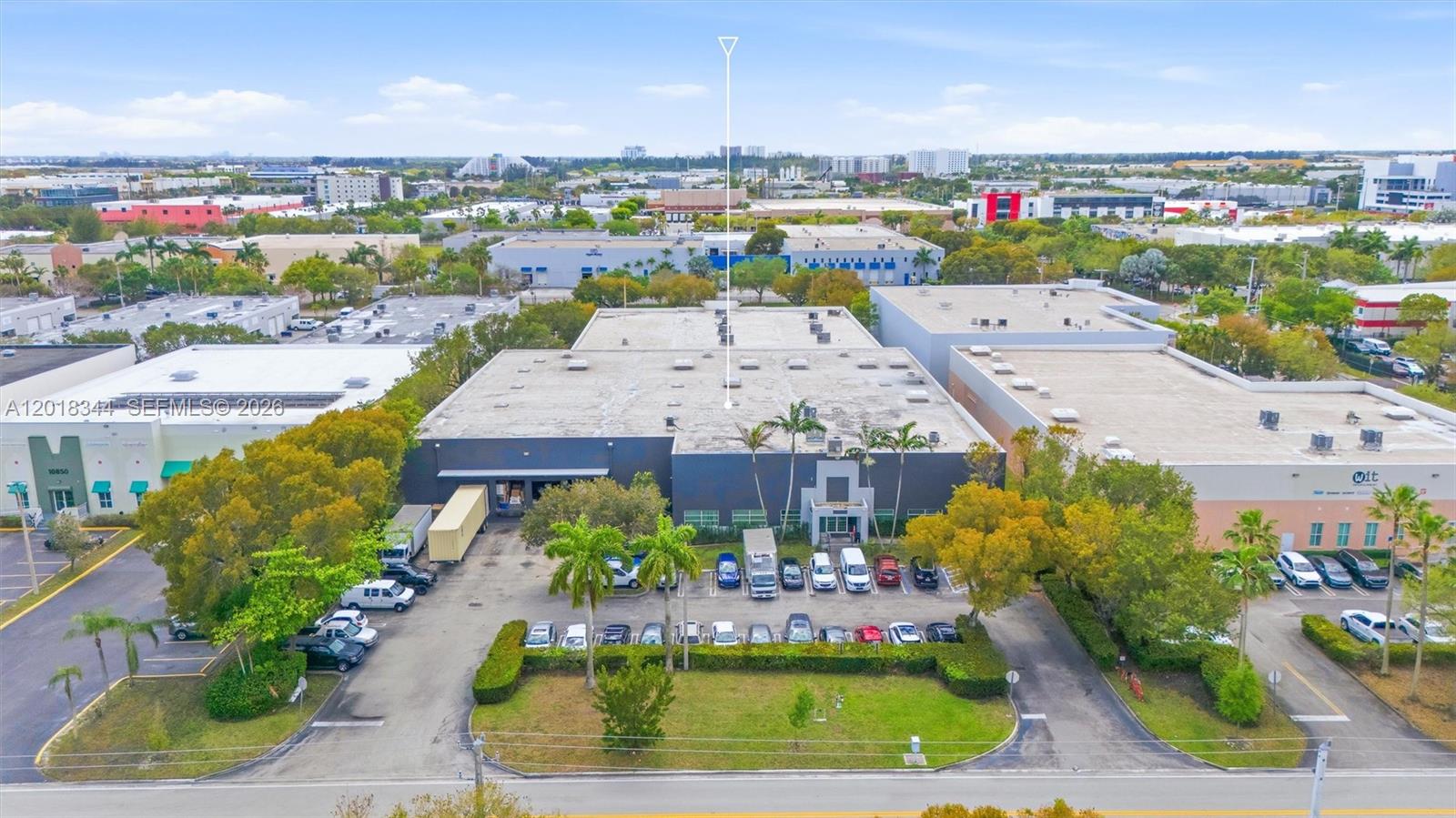 An aerial view shows a commercial warehouse building with a parking lot and surrounding trees — 10880 NW 30th St, Doral FL 33172, DORAL, FL