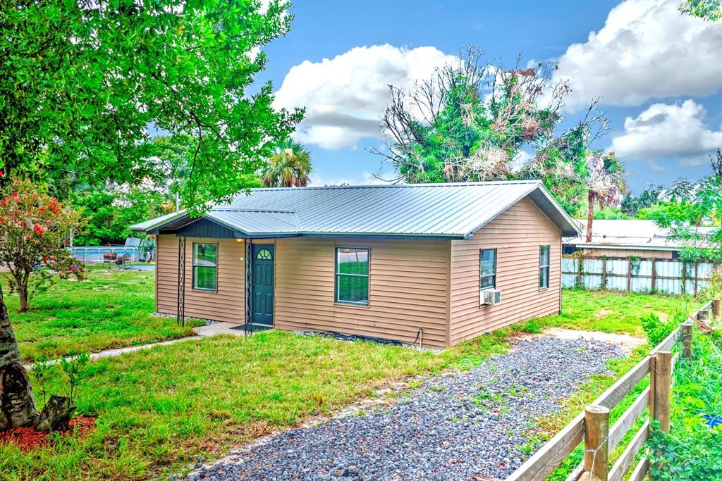 A small, tan, single-story house with a metal roof sits on a gravel driveway — 131 WIGGINS AVENUE, AVON PARK, FL