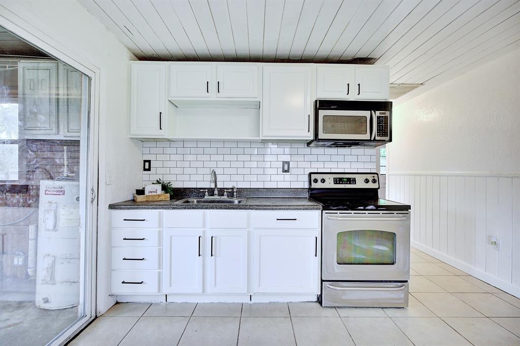 A kitchen features white cabinets, a subway tile backsplash, stainless steel appliances, and tile flooring — 131 WIGGINS AVENUE, AVON PARK, FL