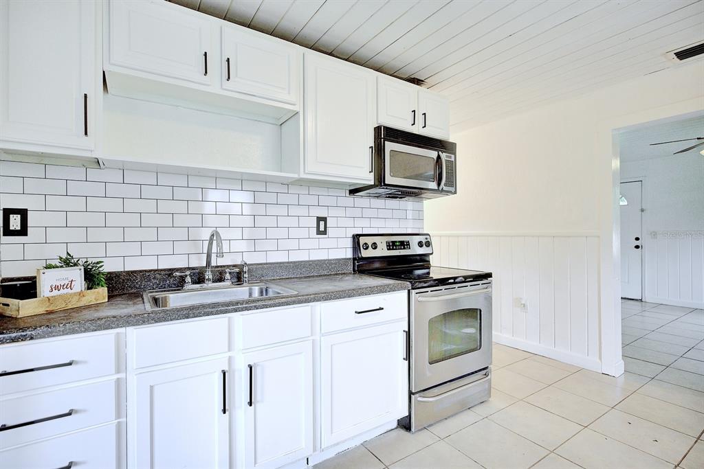 A kitchen features white cabinets, a subway tile backsplash, stainless steel appliances, and tiled flooring — 131 WIGGINS AVENUE, AVON PARK, FL