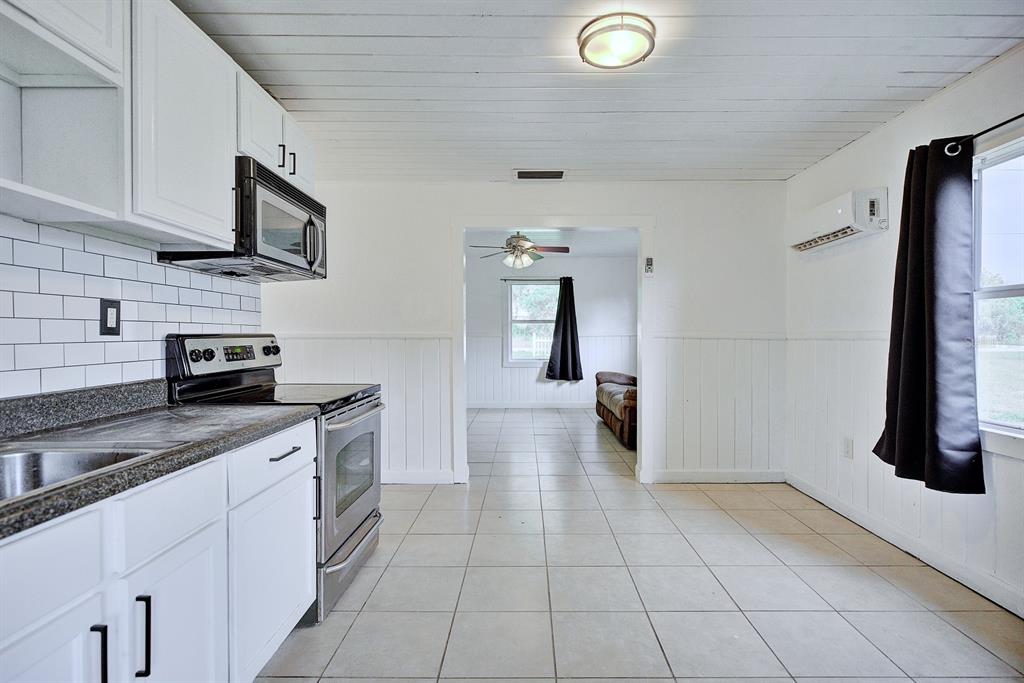 A kitchen with white cabinets, a subway tile backsplash, and tile flooring leads to another room — 131 WIGGINS AVENUE, AVON PARK, FL