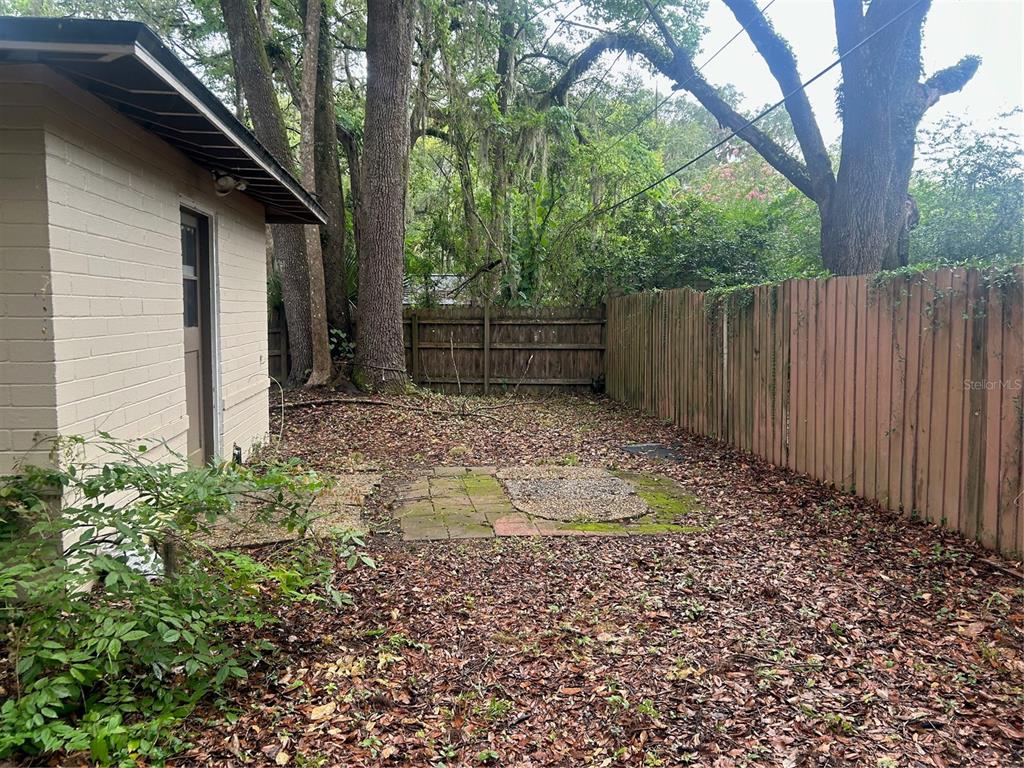 A small backyard features a brick patio, a wooden fence, and a light-colored building — 2704 NW 1ST AVENUE, GAINESVILLE, FL