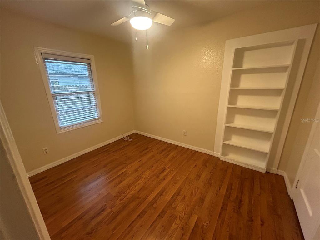 A bedroom with hardwood floors, a ceiling fan, a window with blinds, and built-in shelving — 2704 NW 1ST AVENUE, GAINESVILLE, FL
