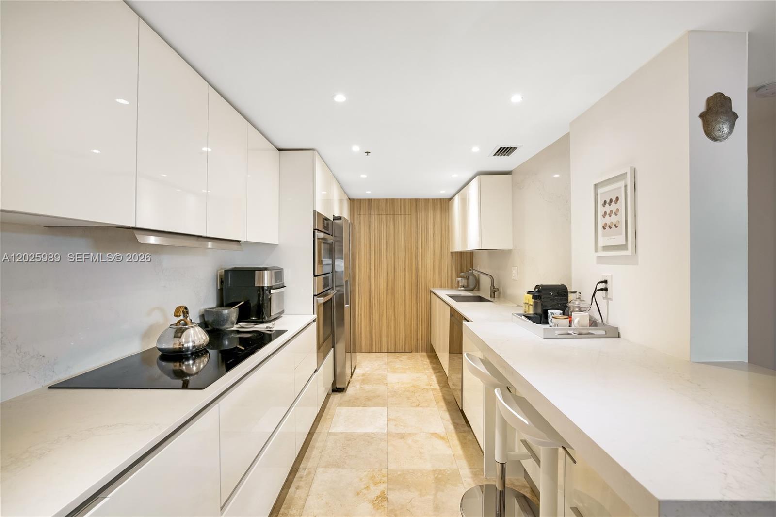A modern galley kitchen features white high-gloss cabinets, stainless steel appliances, and stone countertops — 701 Brickell Key Blvd # 512, Miami FL 33131, MIAMI, FL