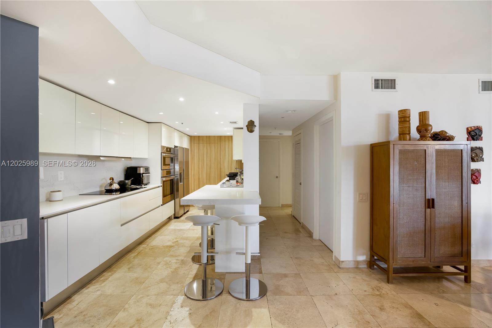 A modern kitchen features white cabinetry, a breakfast bar with stools, and stone tile flooring — 701 Brickell Key Blvd # 512, Miami FL 33131, MIAMI, FL
