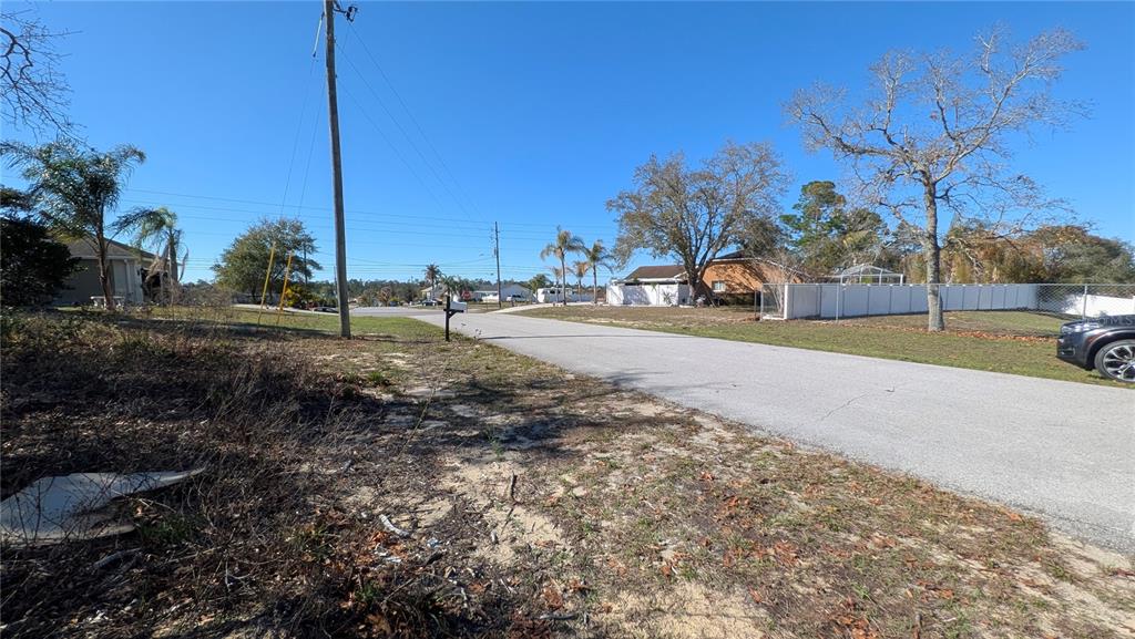 A view of a paved street with a vacant, overgrown lot in the foreground — 13014 HANLEY DRIVE, SPRING HILL, FL