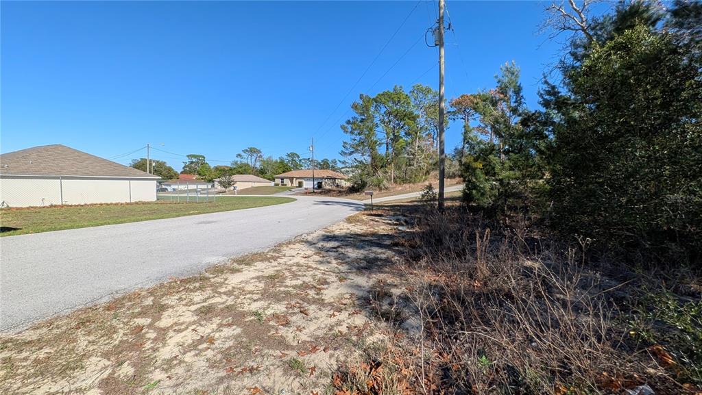 A paved road curves past a vacant, sandy lot with trees and nearby residential houses — 13014 HANLEY DRIVE, SPRING HILL, FL