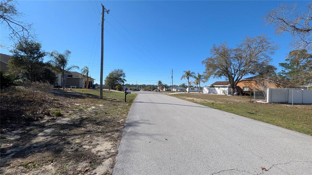 A paved residential street leads toward houses under a clear blue sky — 13014 HANLEY DRIVE, SPRING HILL, FL