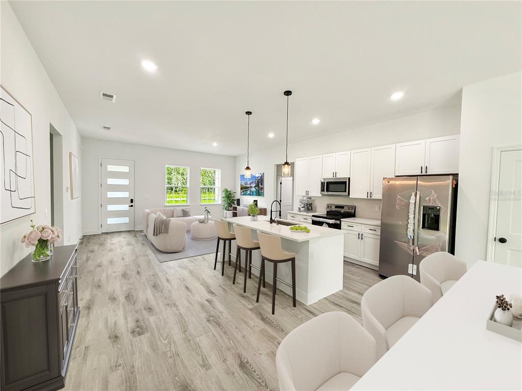 A bright, open-concept kitchen and living area with white cabinetry, a large island, and flooring — 16242 SW 28TH TERRACE, OCALA, FL