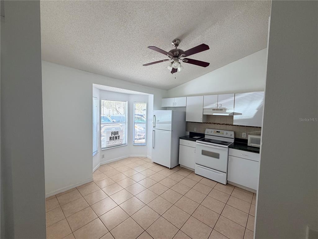 A kitchen with white cabinets, black countertops, tile flooring, and a bay window — 2411 KAM COURT, KISSIMMEE, FL
