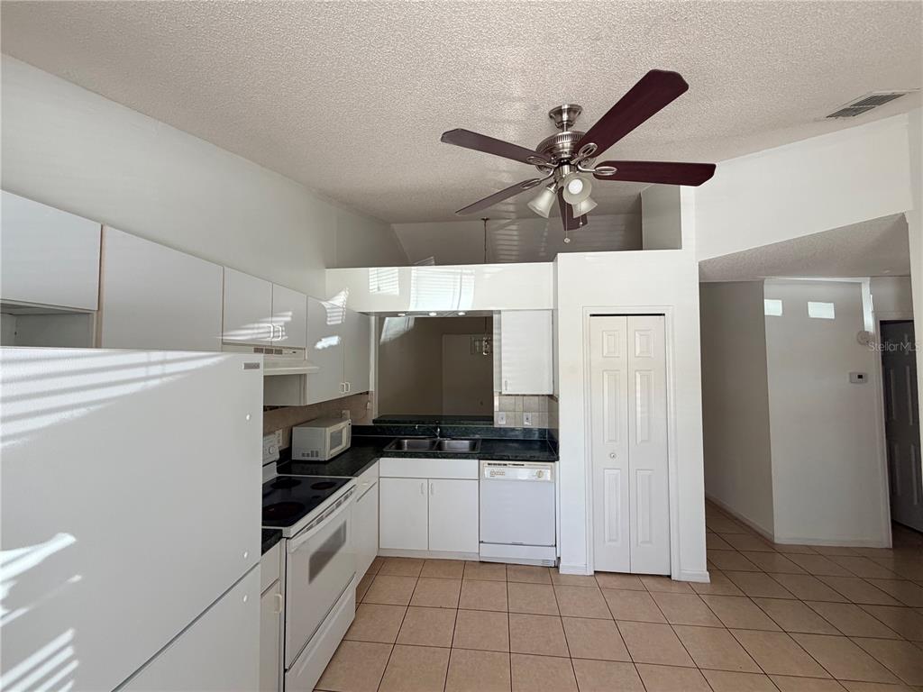 A kitchen features white cabinetry, a ceiling fan, tiled floors, and a pass-through window — 2411 KAM COURT, KISSIMMEE, FL