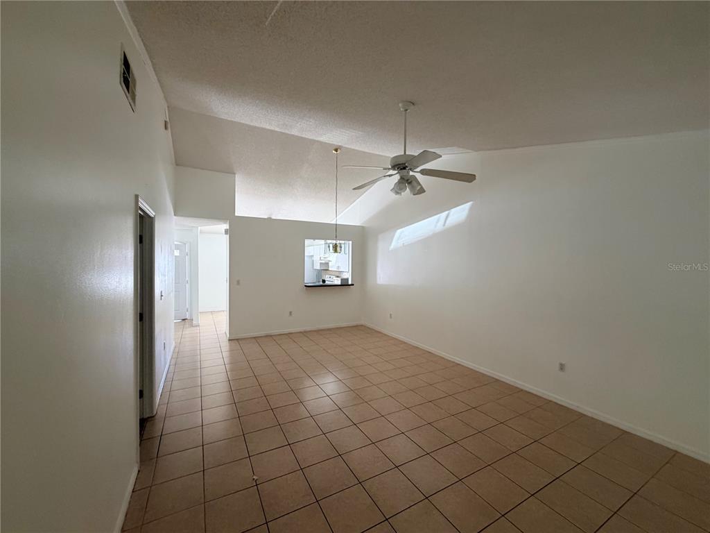 An empty living room features vaulted ceilings, tile flooring, and a pass-through to the kitchen — 2411 KAM COURT, KISSIMMEE, FL