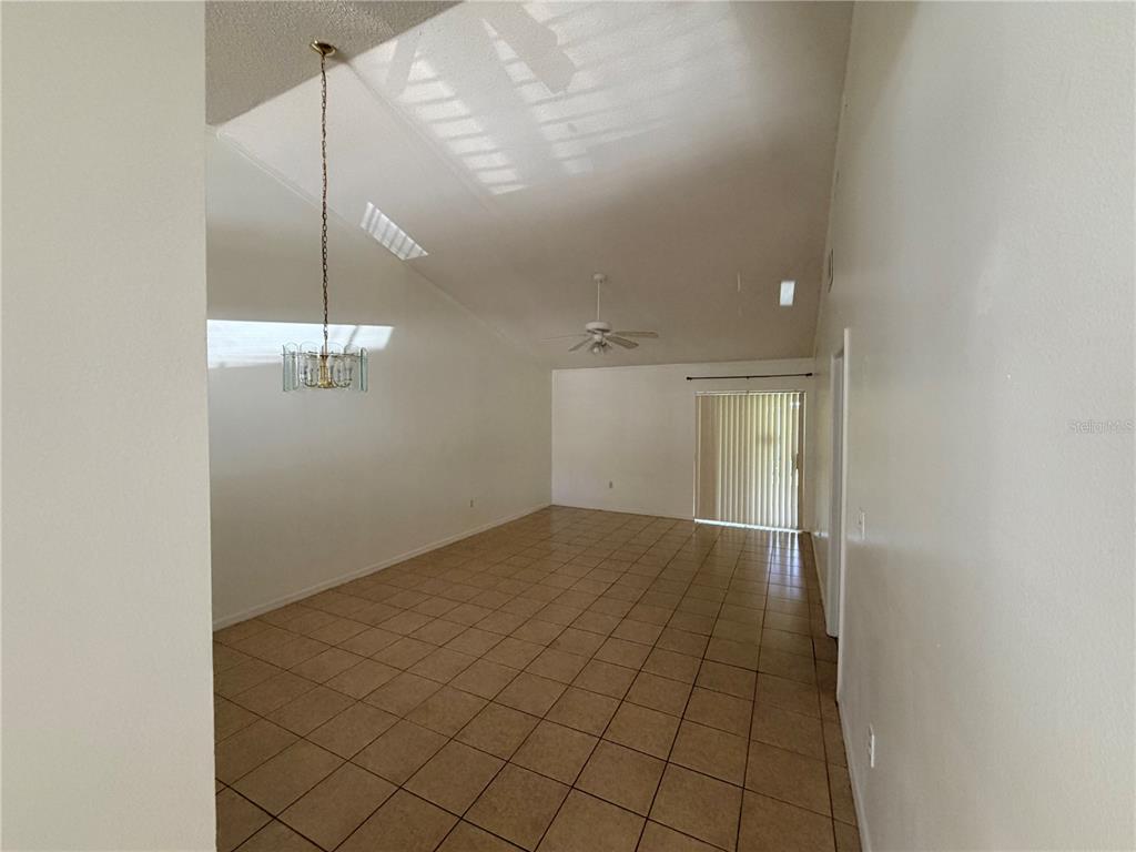 A spacious room with vaulted ceilings, tile flooring, a chandelier, and sliding glass doors — 2411 KAM COURT, KISSIMMEE, FL