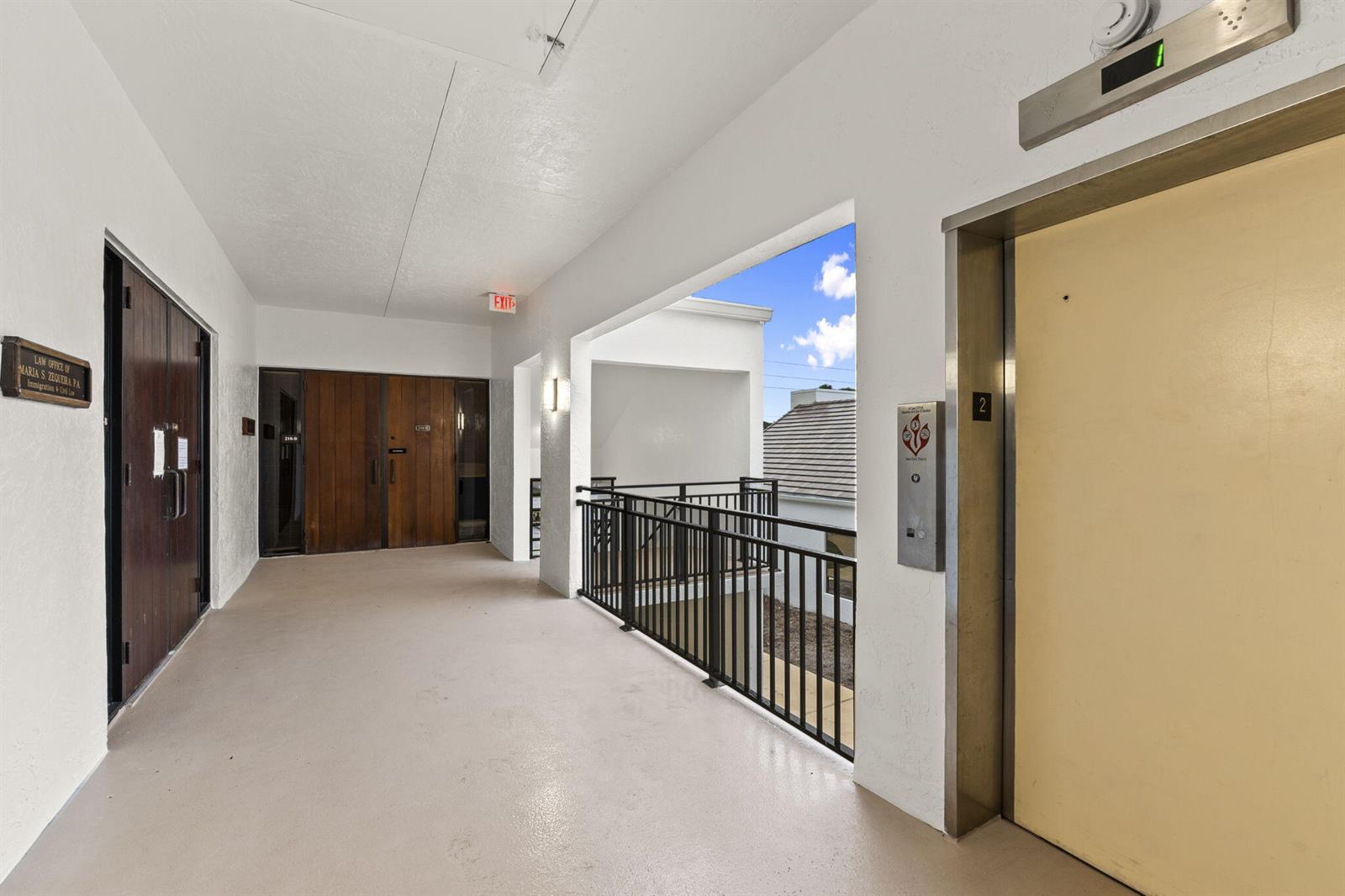 An outdoor hallway features a beige floor, an elevator, and a dark wooden door — 900 SE Ocean Boulevard # B212, Stuart FL 34994, STUART, FL