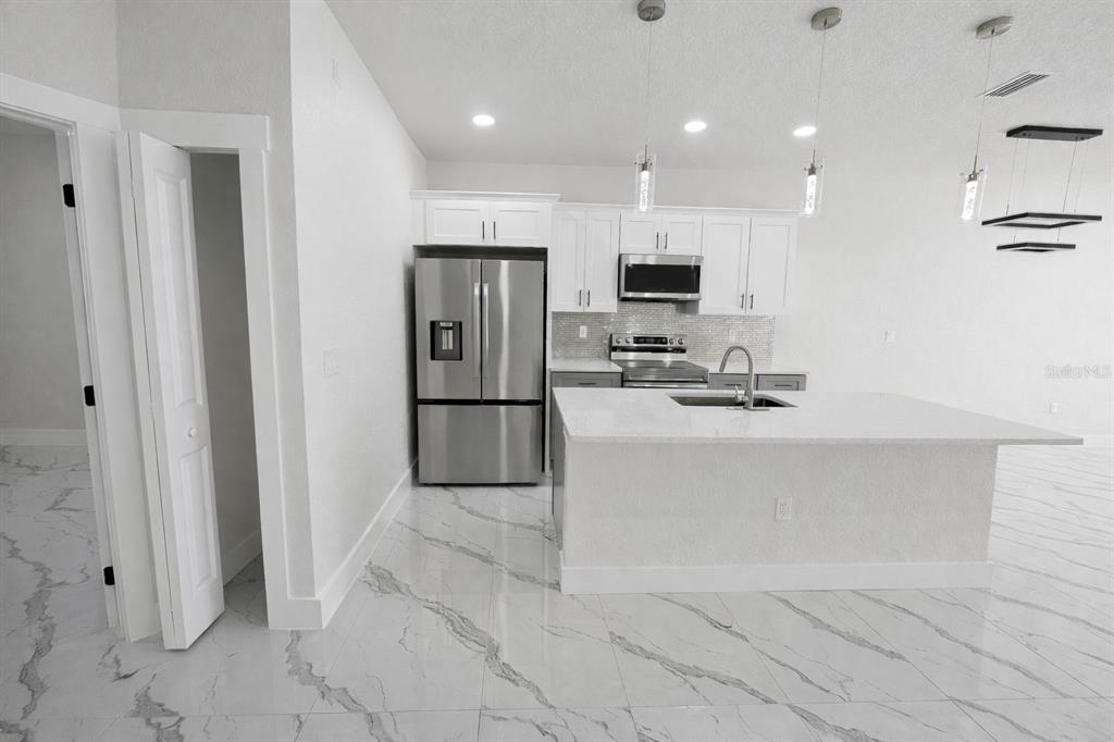 A modern kitchen features white cabinetry, stainless steel appliances, a center island, and marble-patterned flooring — 4820/4822 24TH STREET SW, LEHIGH ACRES, FL