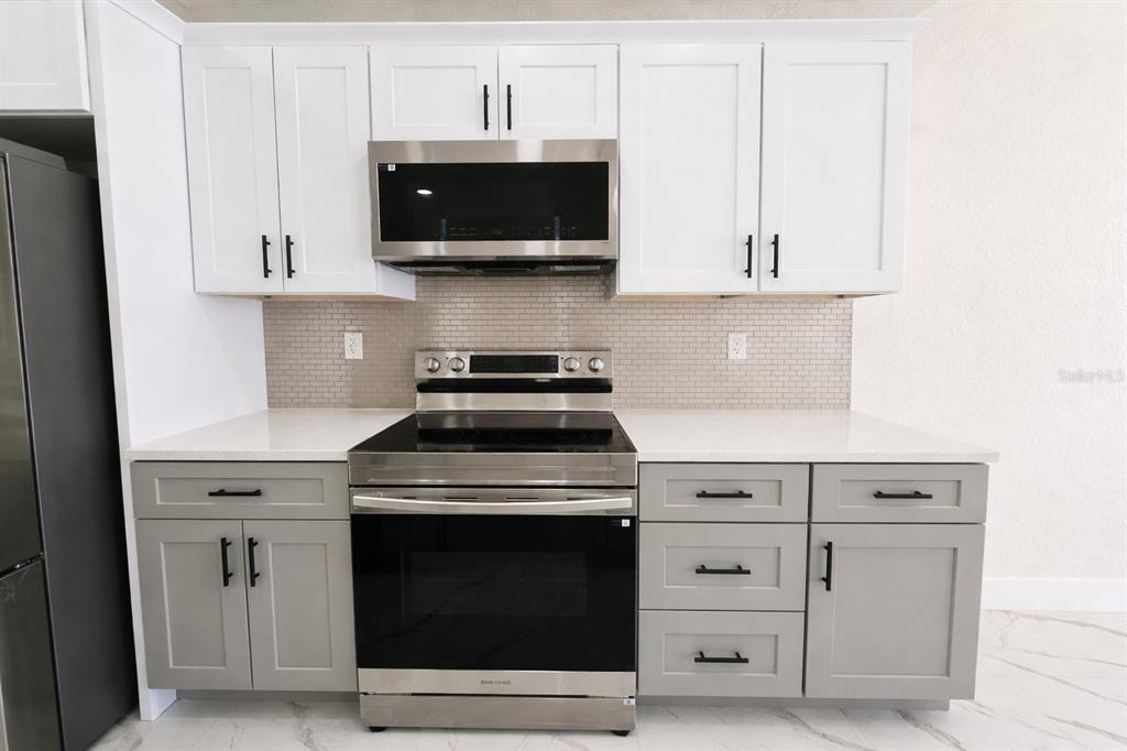 A kitchen features white upper cabinets, gray lower cabinets, stainless steel appliances, and a backsplash — 4820/4822 24TH STREET SW, LEHIGH ACRES, FL