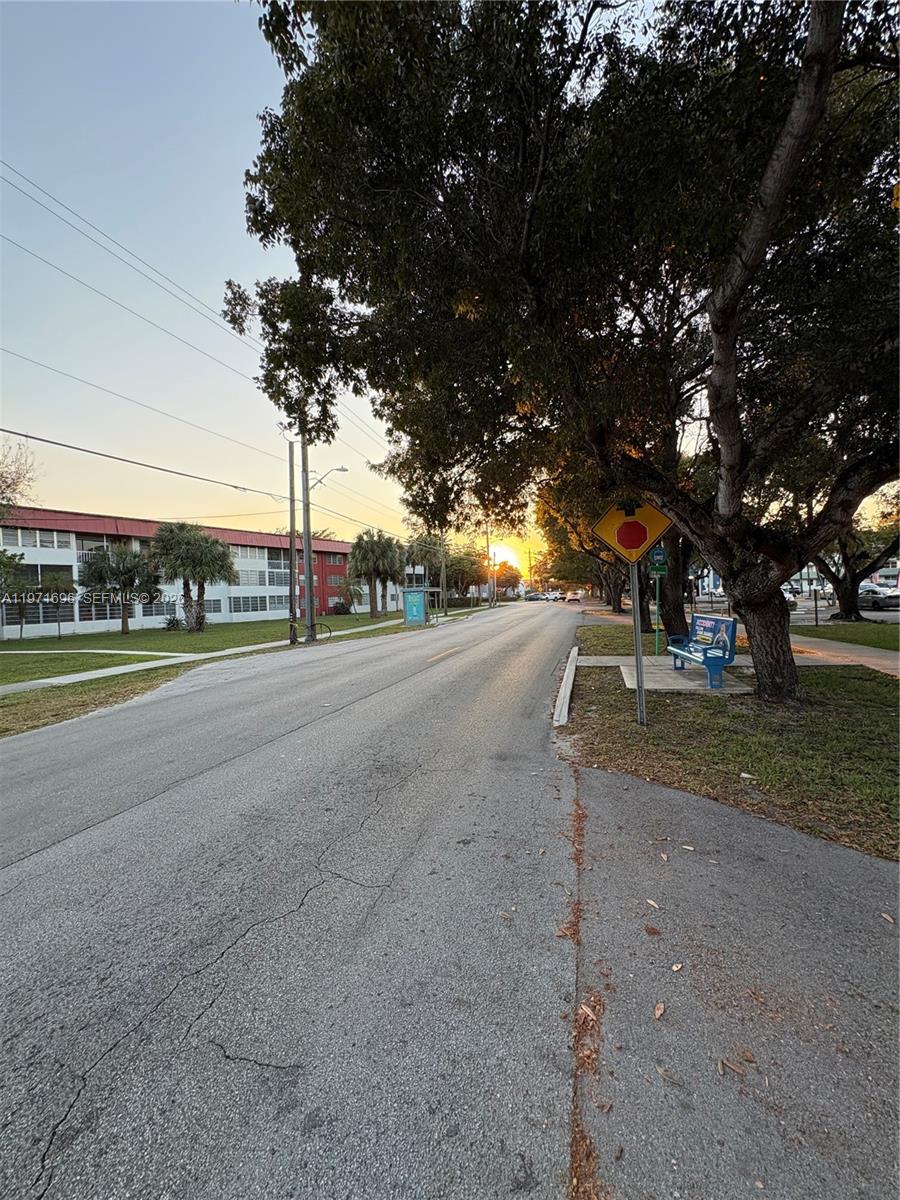 A street view shows a road, a bus stop bench, and trees at sunset — 1401 NE 191st St # D204, Miami FL 33179, MIAMI, FL