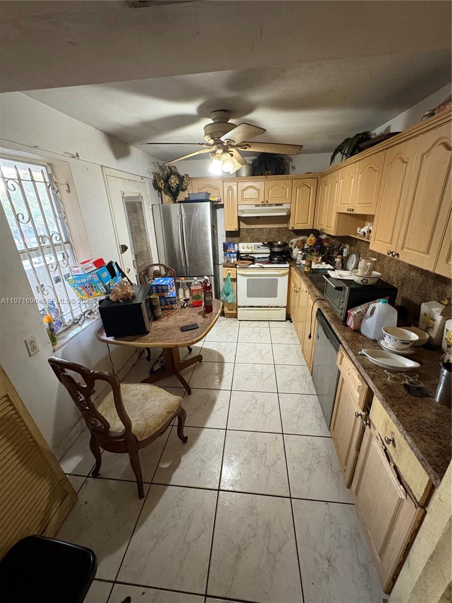 A kitchen features light wood cabinets, a small dining table, and white tile flooring — 1401 NE 191st St # D204, Miami FL 33179, MIAMI, FL