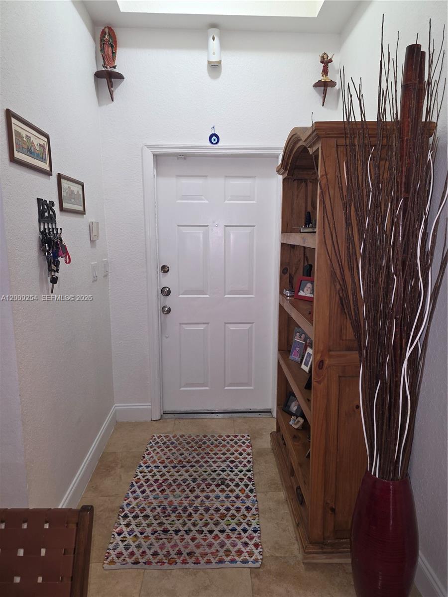 An entryway features a white door, a wooden bookshelf, a patterned rug, and wall decor — 12454 SW 123rd St, Miami FL 33186, MIAMI, FL