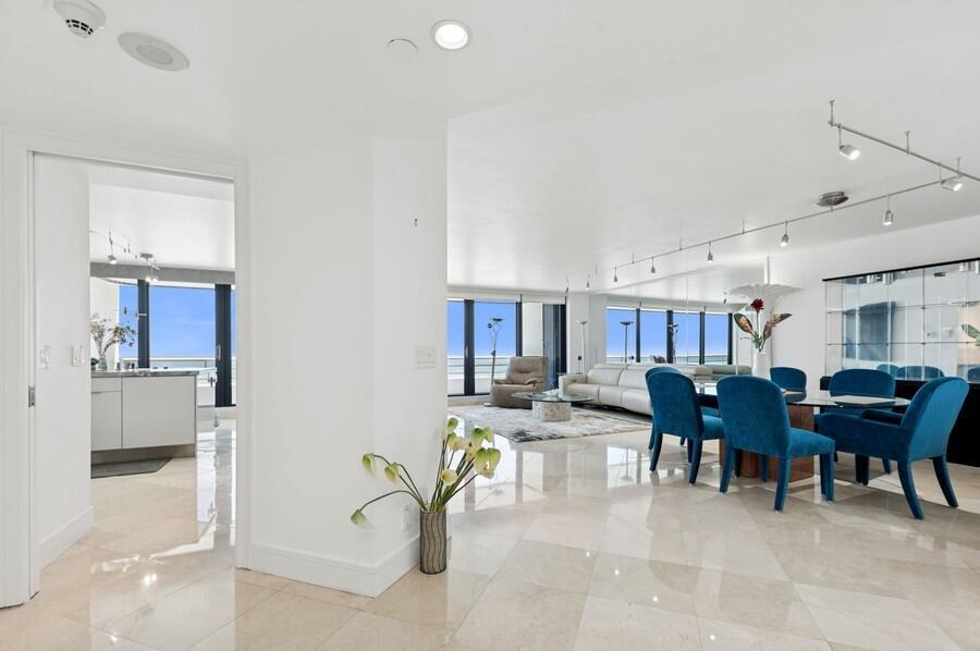 An open-concept living and dining area with marble floors, blue chairs, and floor-to-ceiling windows — 1400 S Ocean Boulevard # 1004, Boca Raton FL 33432, BOCA RATON, FL