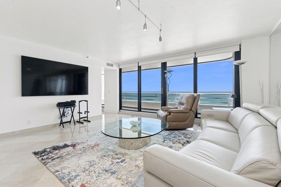 A living room features a white leather sofa, glass coffee table, and ocean view windows — 1400 S Ocean Boulevard # 1004, Boca Raton FL 33432, BOCA RATON, FL