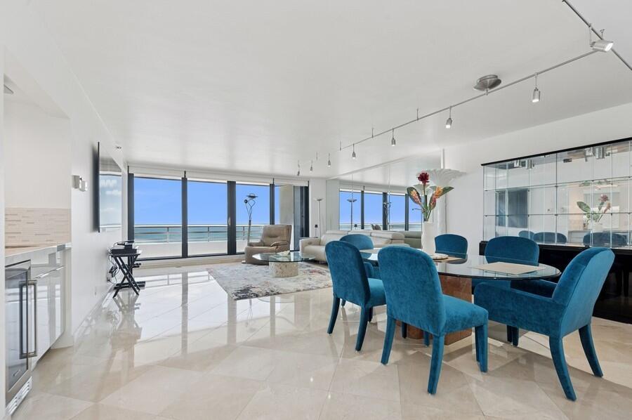 A bright living and dining area with marble floors, blue chairs, and a balcony view — 1400 S Ocean Boulevard # 1004, Boca Raton FL 33432, BOCA RATON, FL