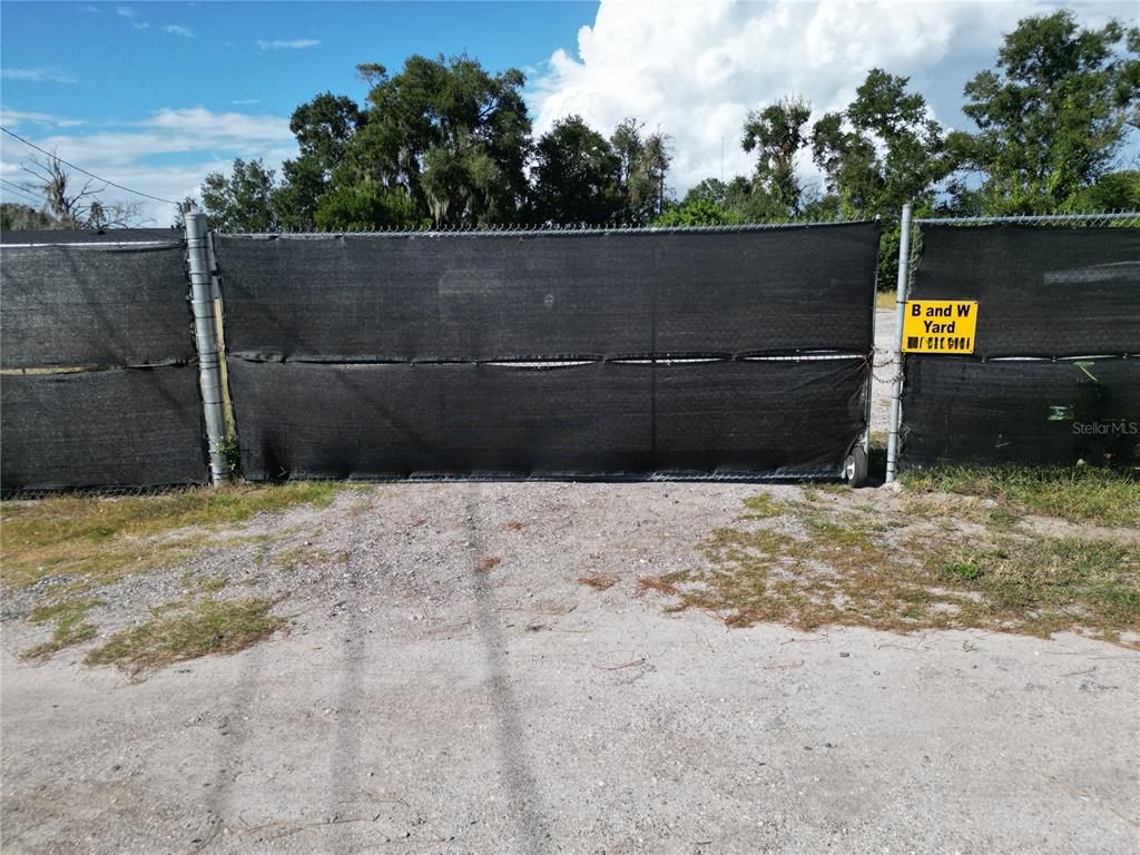 A black privacy screen covers a chain-link gate at the entrance to a gravel lot — 4155 PINE HAVEN ROAD, NEW PORT RICHEY, FL