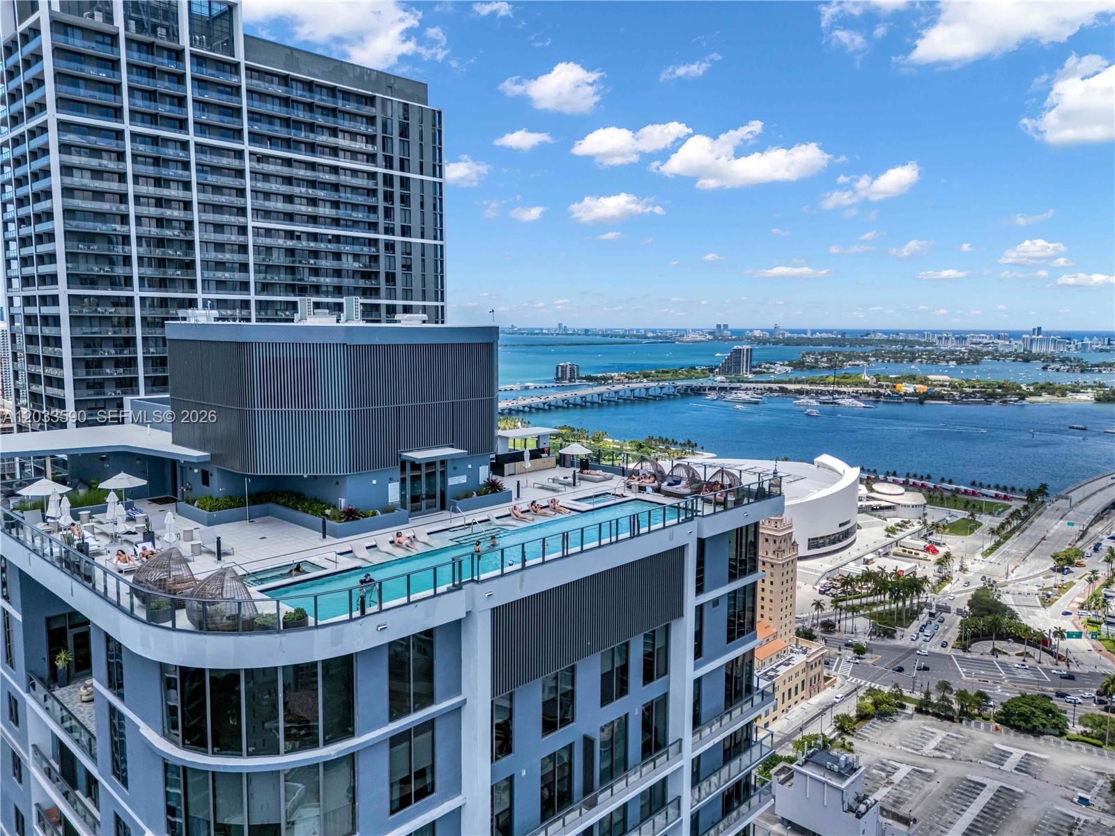 An aerial view shows a rooftop swimming pool on a high-rise building overlooking the bay — 121 NE 5th St # 1400, Miami FL 33132, MIAMI, FL