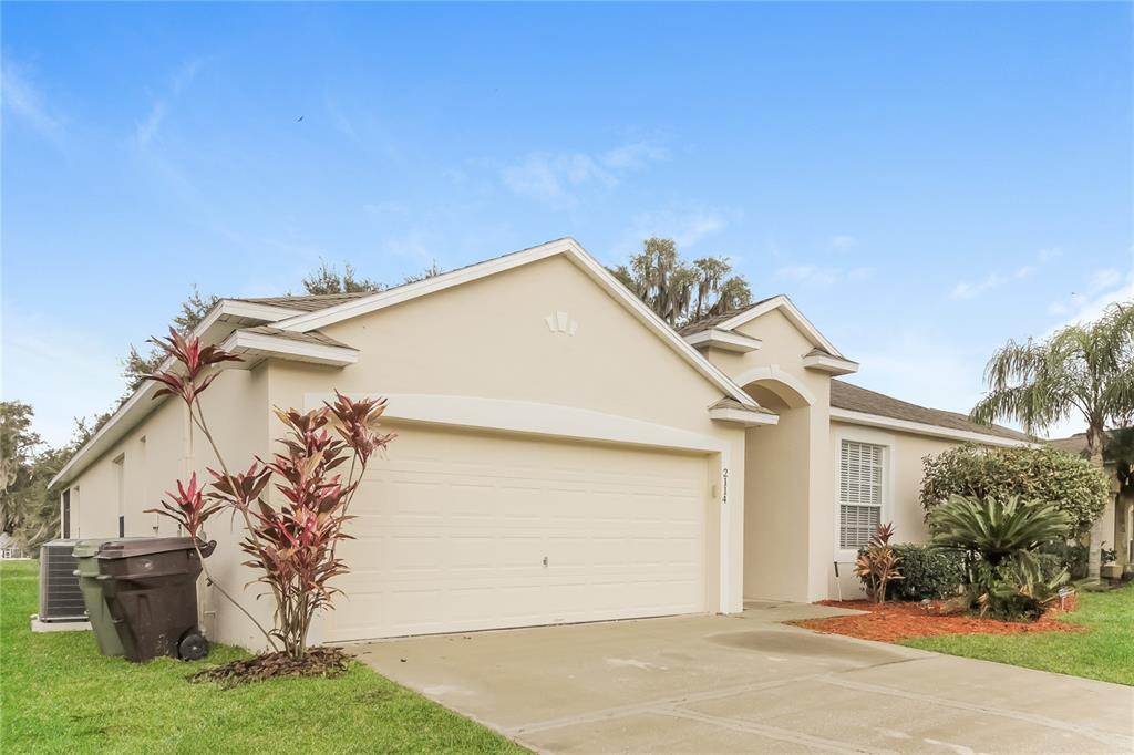 A beige single-story house with a two-car garage and a concrete driveway — 2114 THE OAKS BOULEVARD, KISSIMMEE, FL