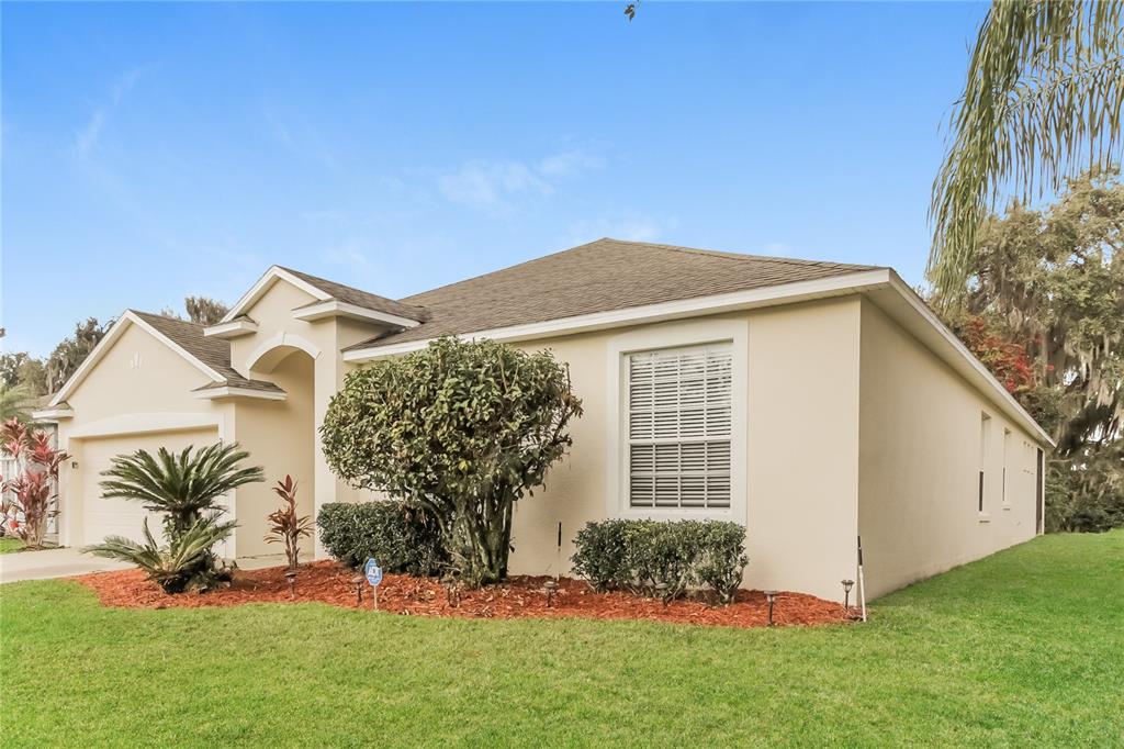 A single-story house with a tan stucco exterior, a shingled roof, and a landscaped yard — 2114 THE OAKS BOULEVARD, KISSIMMEE, FL