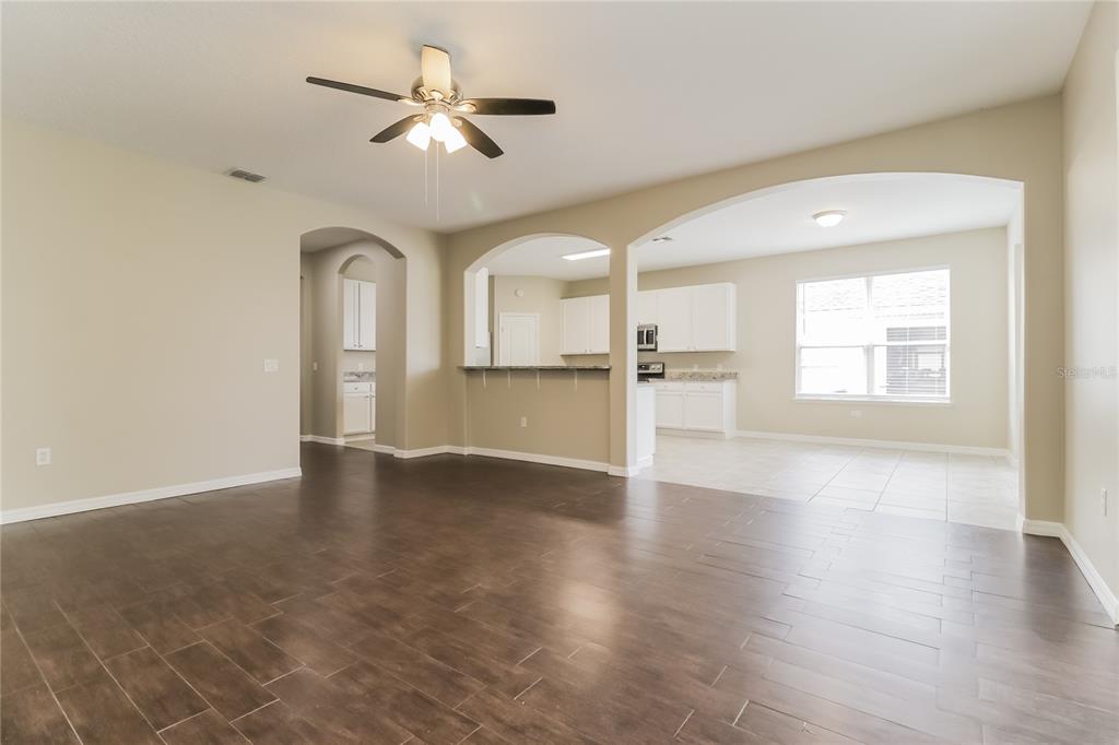 A spacious living room with dark wood-look tile floors opens to a white kitchen — 2114 THE OAKS BOULEVARD, KISSIMMEE, FL