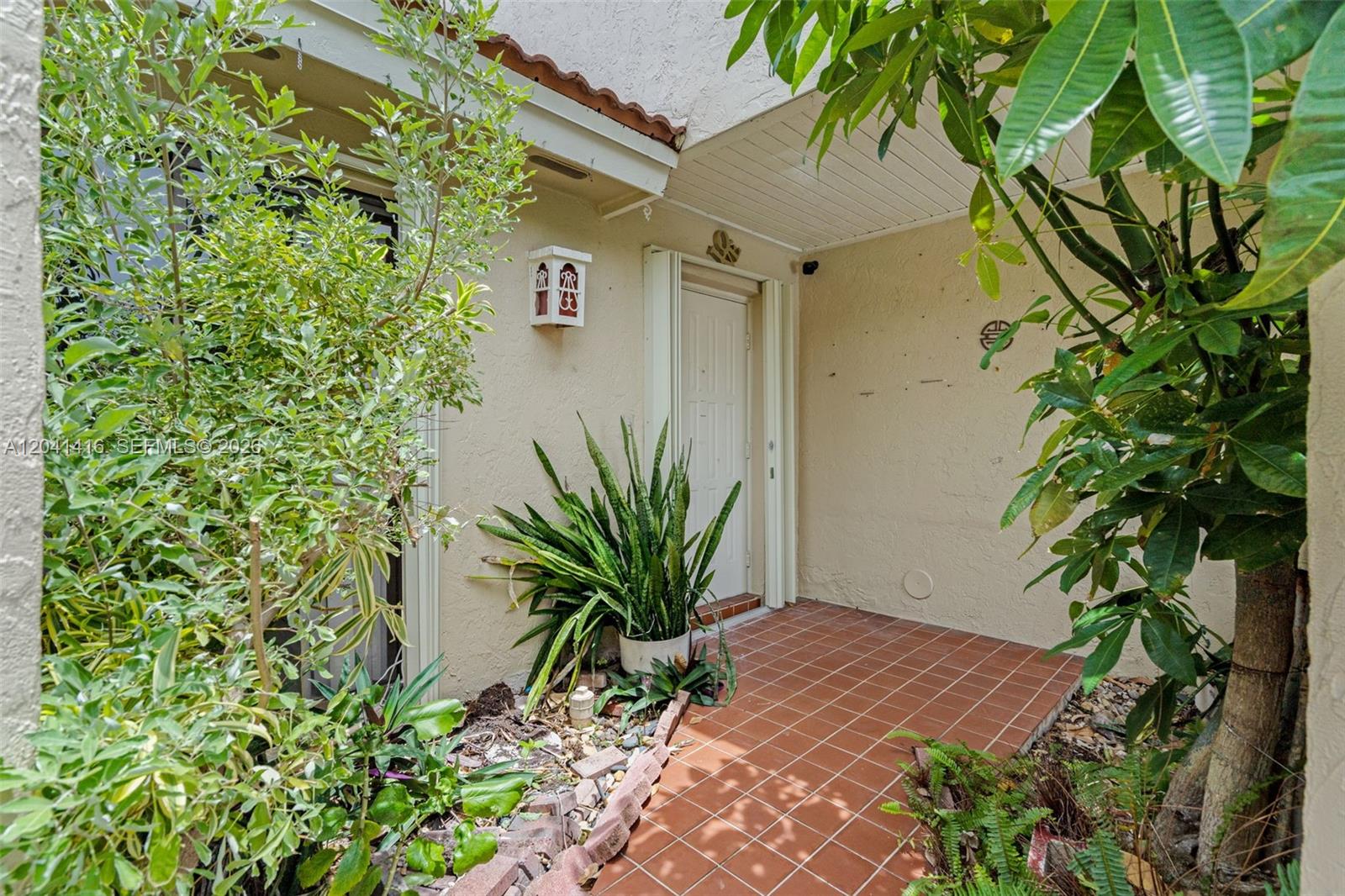 A tiled entryway leads to a white front door surrounded by lush potted plants — 6233 NW 170th Ter, Miami FL 33015, MIAMI, FL