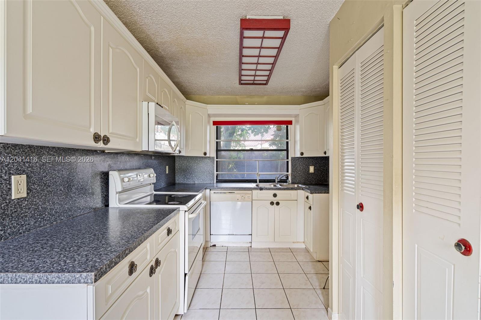 A kitchen features white cabinets, dark speckled countertops, a white stove, and tiled flooring — 6233 NW 170th Ter, Miami FL 33015, MIAMI, FL