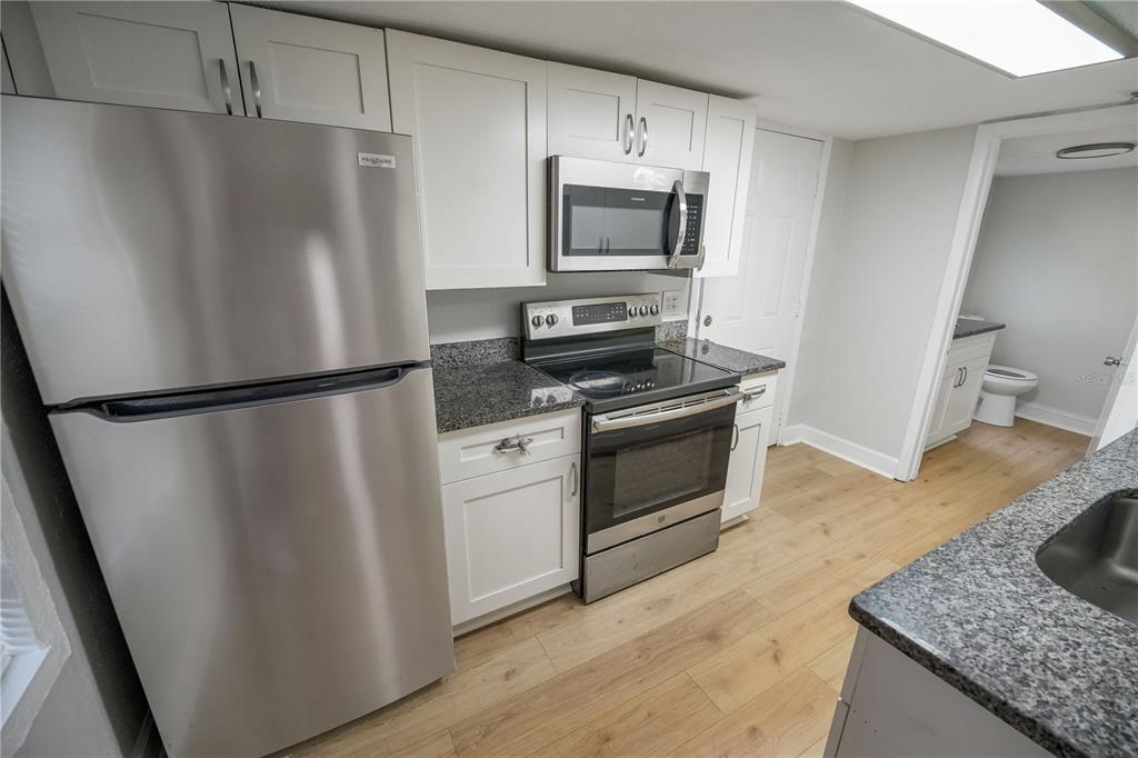 A kitchen features stainless steel appliances, white cabinets, and granite countertops with light wood flooring — 8103 N BROOKS STREET, TAMPA, FL